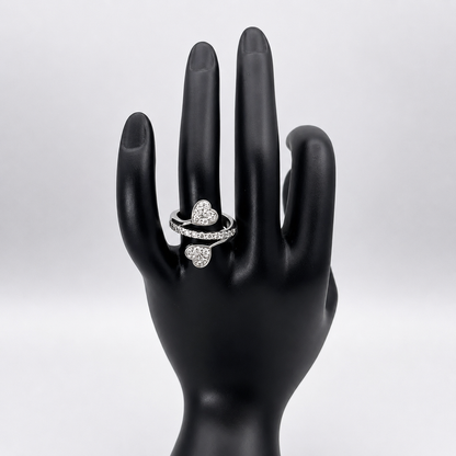 A silver ring with three heart-shaped pavé settings, displayed on a black mannequin hand against a light gray background.