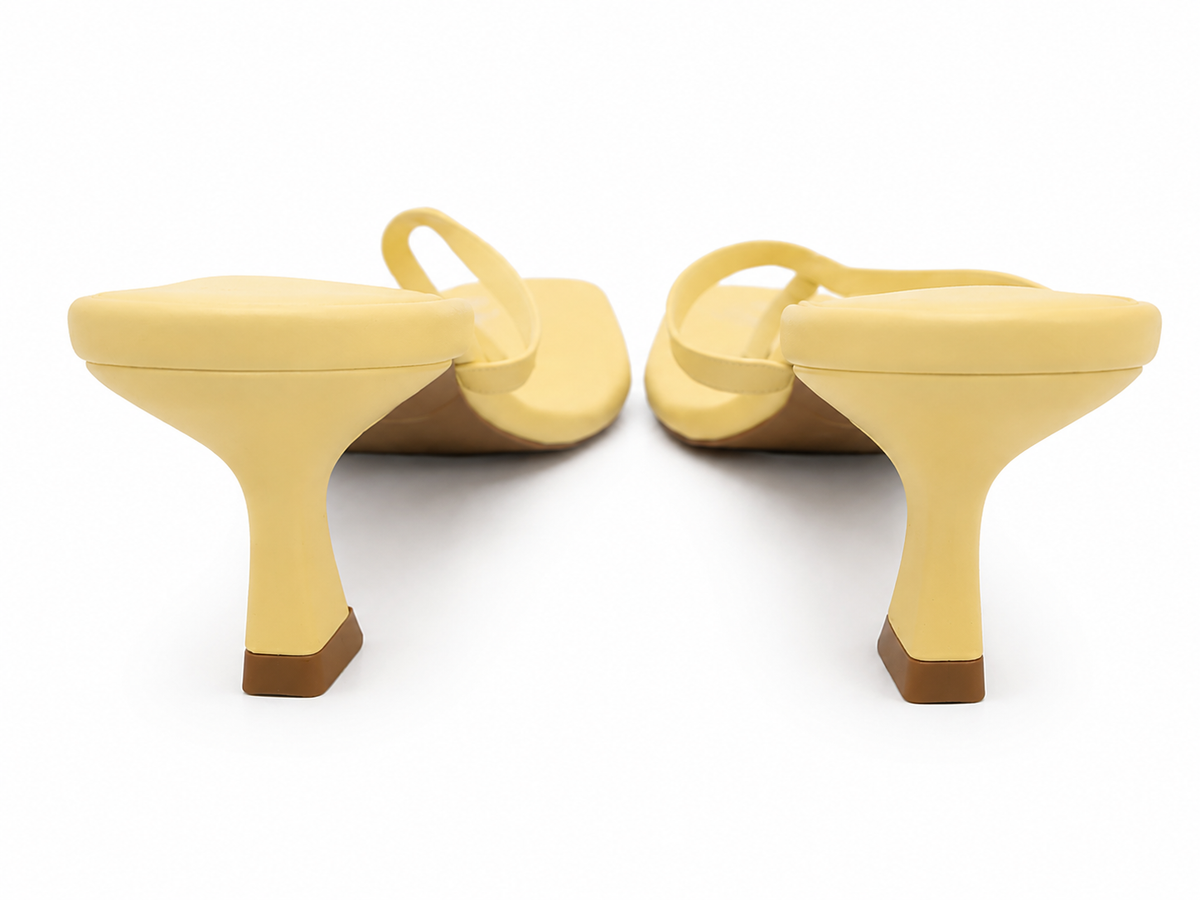A pair of pale yellow heeled sandals shown from the back on a clean white background.