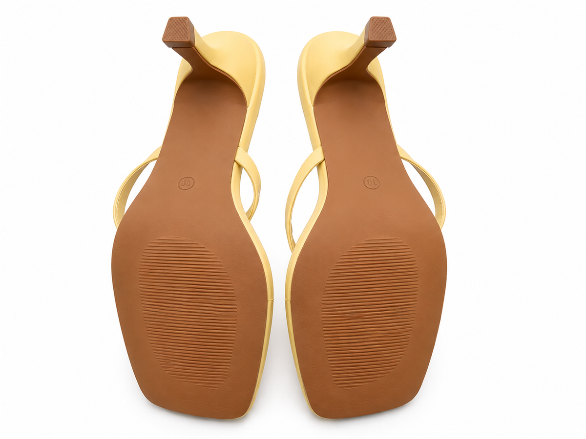 A pair of women's flat sandals shown from the bottom, featuring a tan-brown sole with a ribbed tread pattern, a light beige footbed, and thin light yellow straps with matching heel caps.