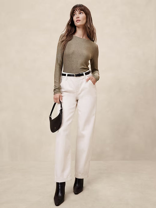 Woman wearing a green sweater and white pants against a beige background