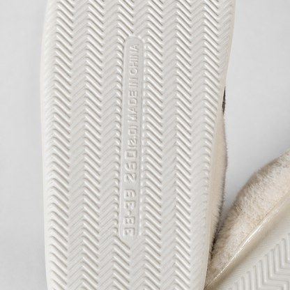 Close-up of the white textured sole of a slip-on shoe, showing the embossed vertical text 'MADE IN CHINA' and 'GB/T 31022-2015', with a soft cream-colored fuzzy material visible along the side.
