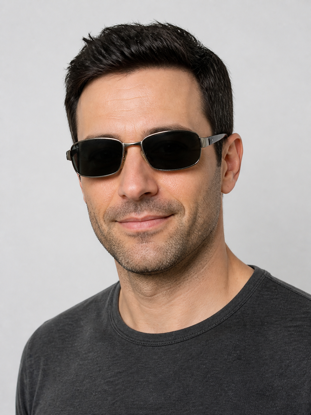 A man wearing slim silver-framed sunglasses with dark lenses, shown from the chest up against a light gray background.