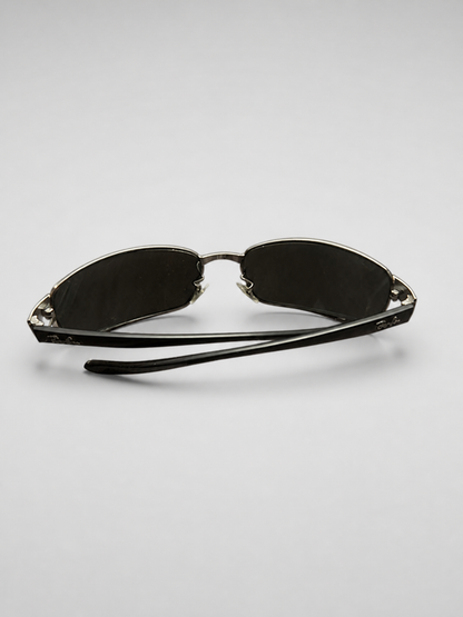 A pair of sunglasses with dark lenses and black temples, featuring decorative silver-toned metal details on the outer edges of the frames, shown on a light gray background.