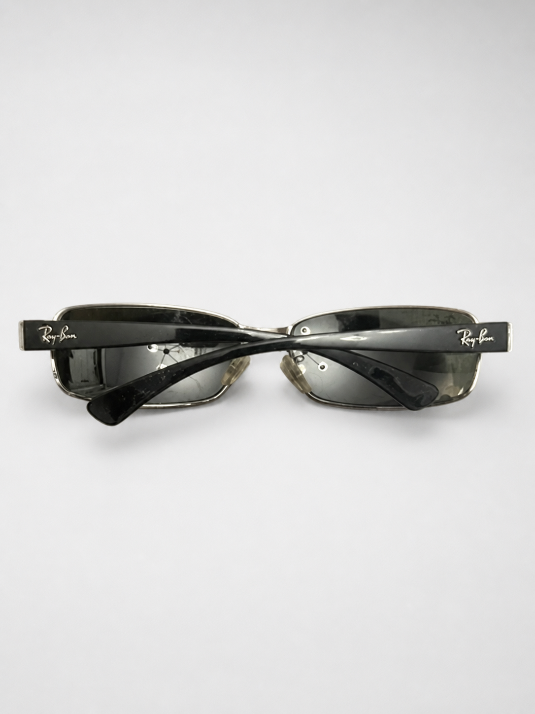 Ray-Ban square rimless sunglasses with dark gray lenses and black acetate arms, displayed on a light gray background.