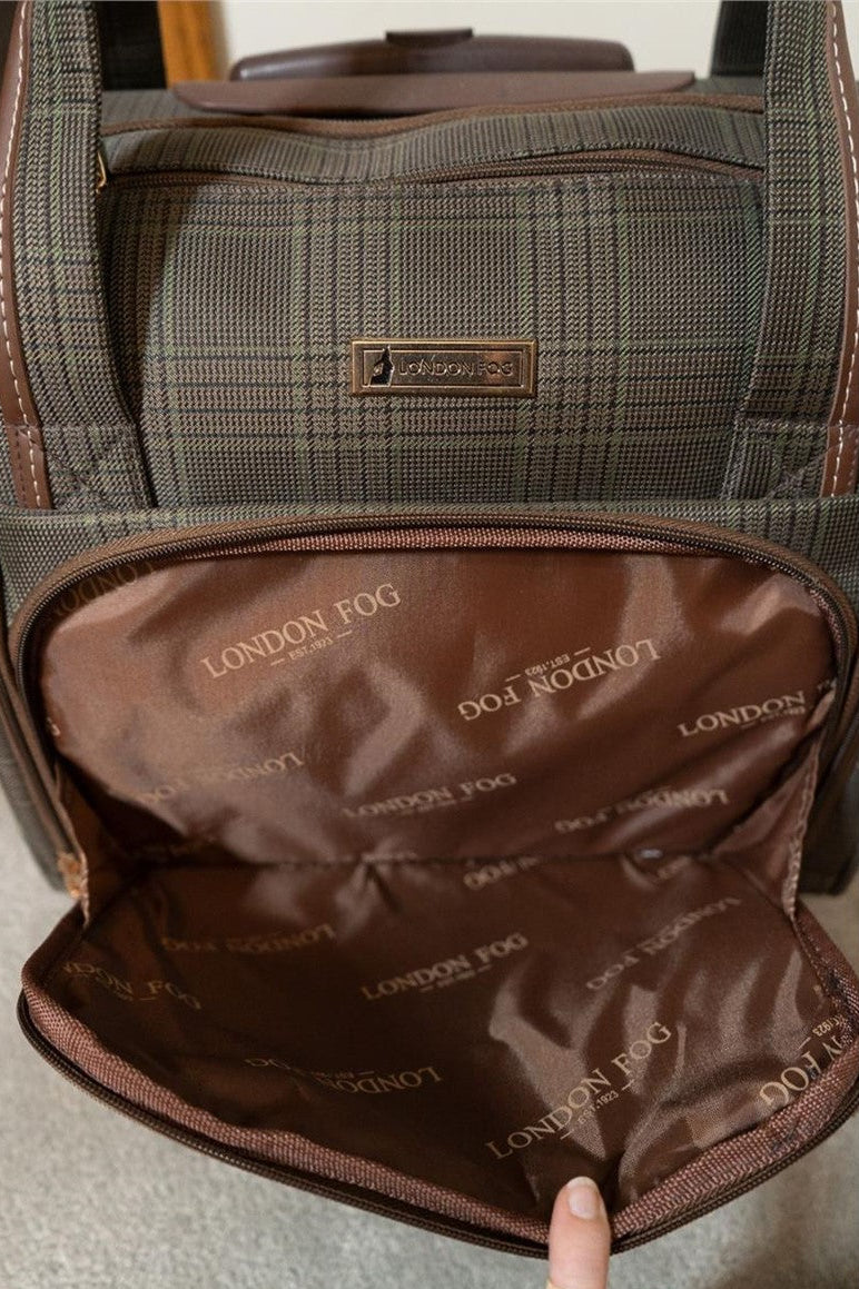 A close-up of a London Fog rolling suitcase showing the brown plaid exterior fabric and the interior compartment with a brown lining printed with the London Fog logo. A finger is pointing at the interior.