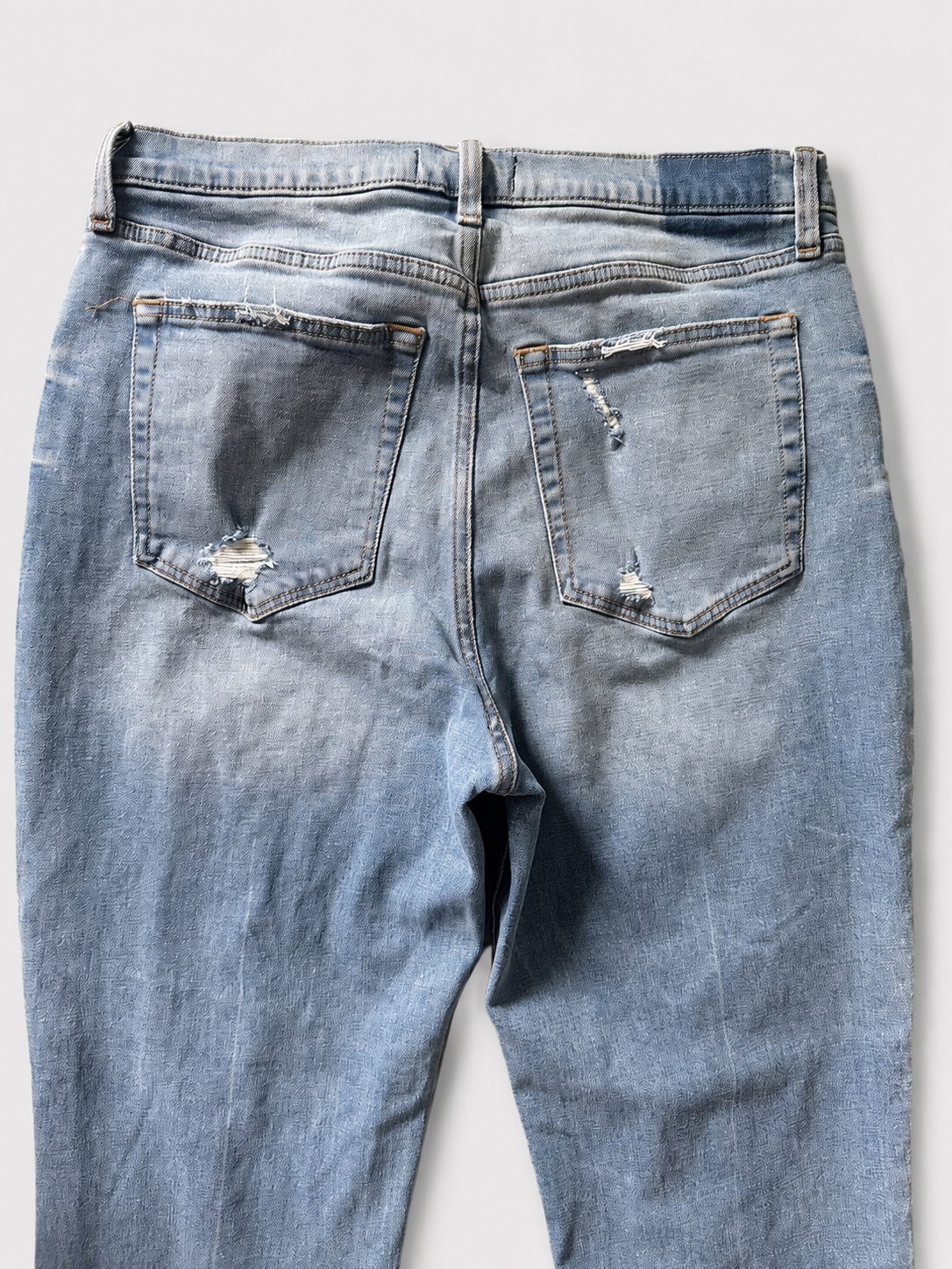 Light blue denim jeans shown from the back, featuring distressed rips on both back pockets and a faded wash.