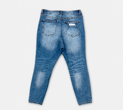 Back view of blue denim jeans with a slim fit, featuring whiskering, fading, and a distressed patch on the right back pocket, set against a plain light gray background.