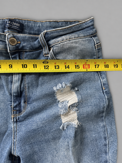 Close-up of a pair of light blue distressed denim jeans laid flat on a gray background, with a yellow measuring tape horizontally positioned across the thigh to show the fabric width.