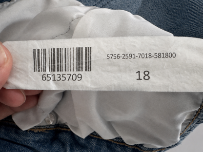 Close-up of a garment's interior size label showing the number 18, barcode, and product code, with blue denim fabric visible around it.