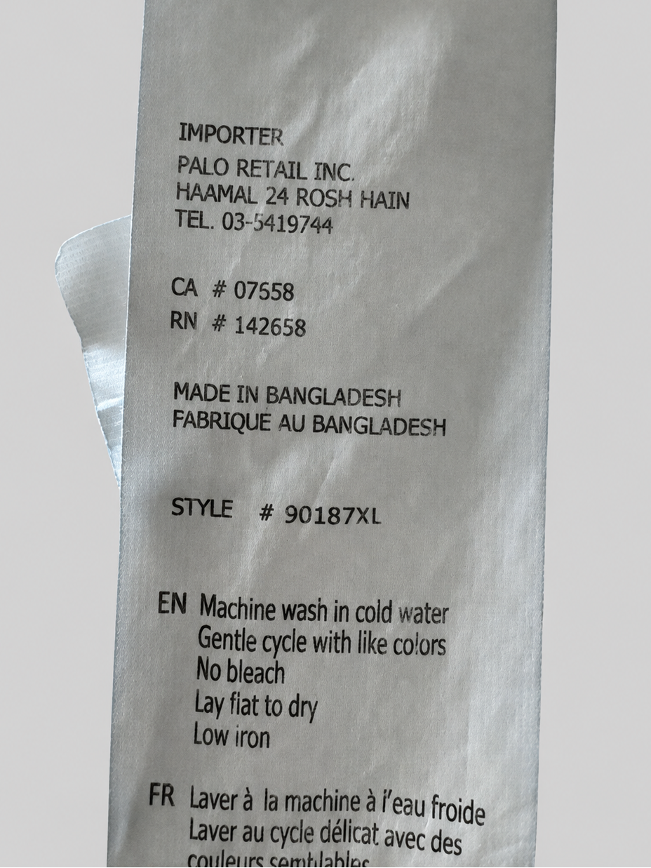 A close-up of a white paper garment care label with black printed text, photographed against a light gray background.