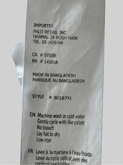 A close-up of a white paper garment care label with black printed text, photographed against a light gray background.