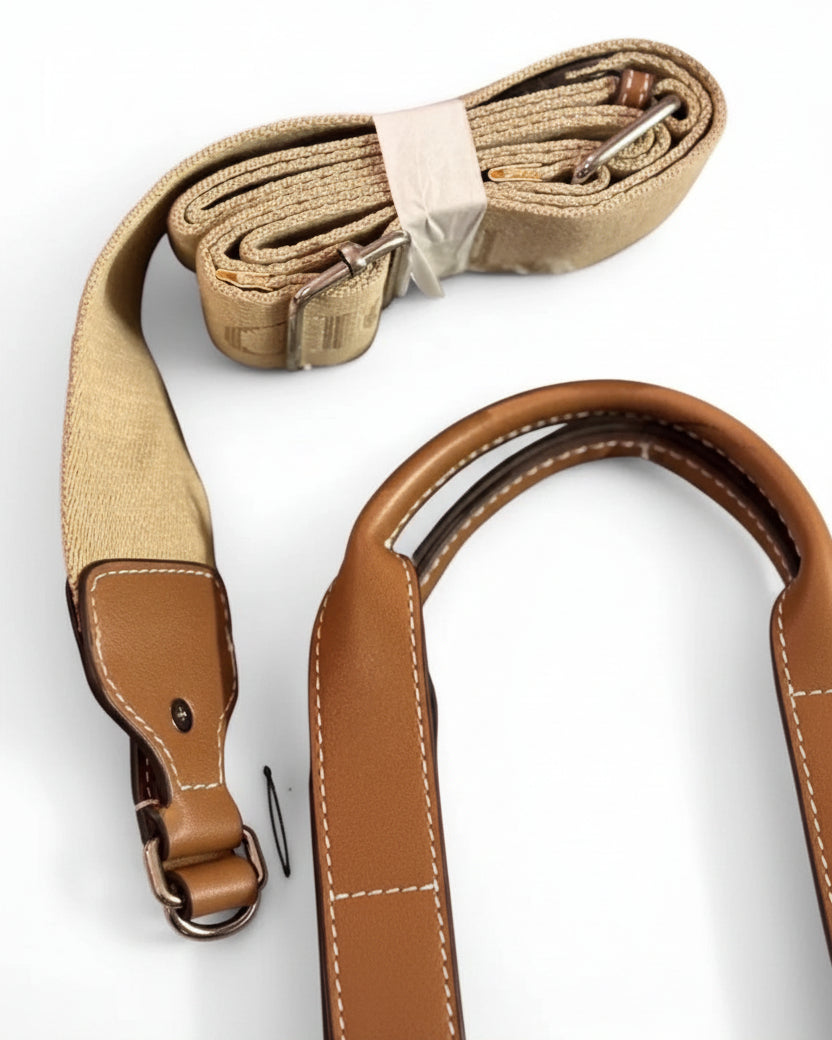 A rolled tan canvas camera strap with brown leather trim and silver metal clips, shown on a plain white background.
