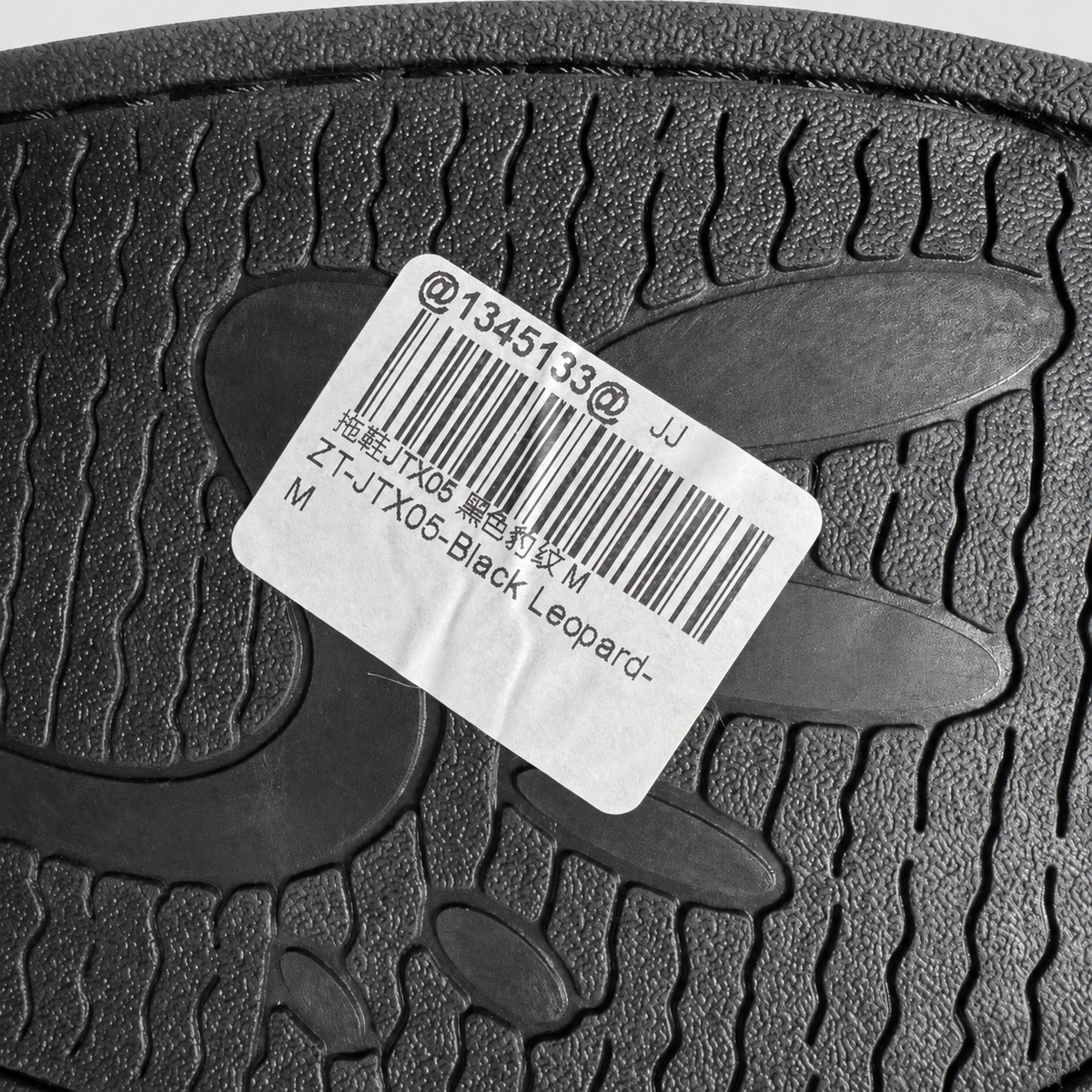 Close-up of a black textured rubber sole with a white product label showing a barcode and text including 'Black Leopard'.