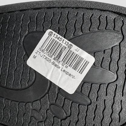 Close-up of a black textured rubber sole with a white product label showing a barcode and text including 'Black Leopard'.