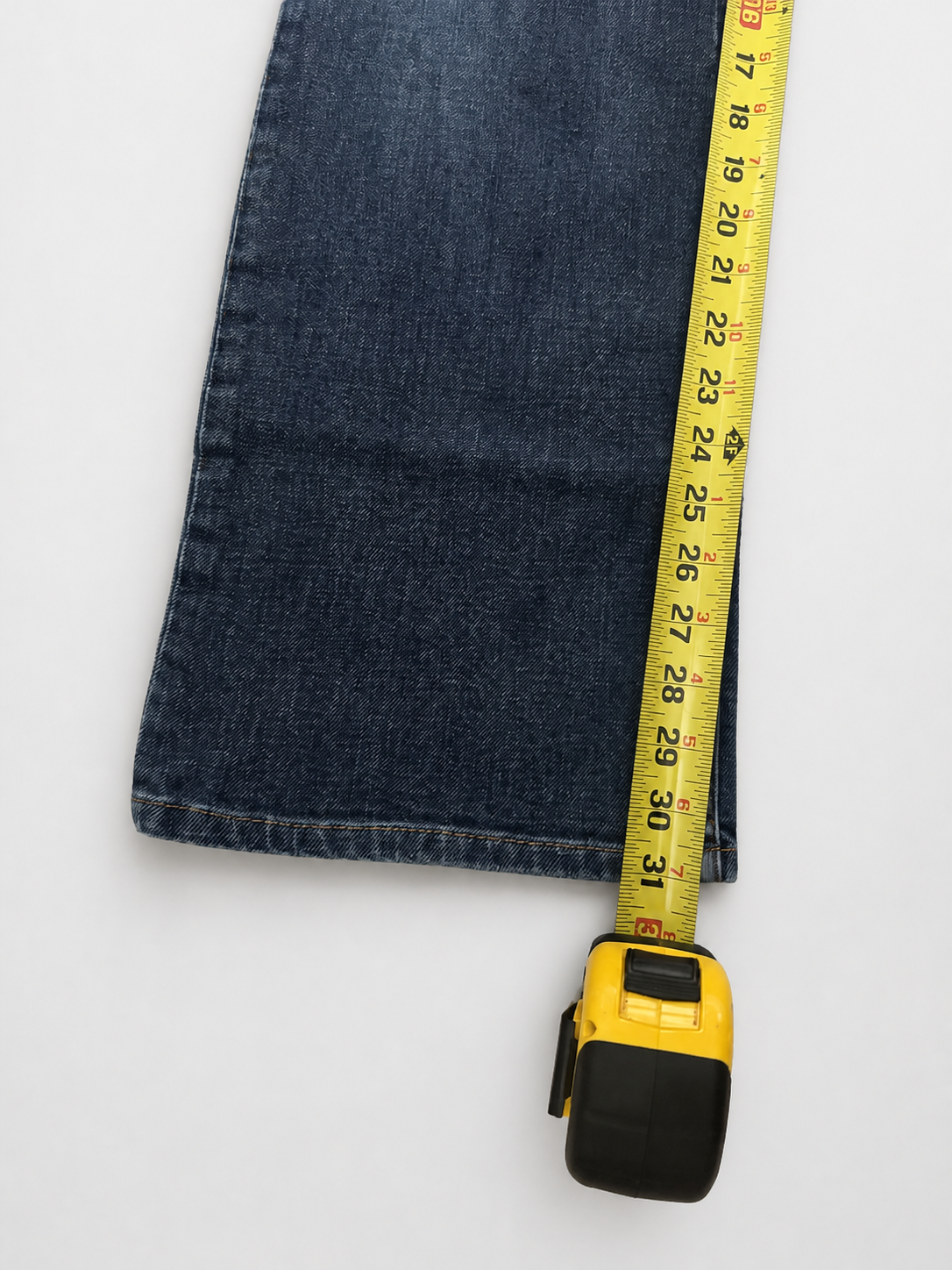 A yellow tape measure extended horizontally over a folded dark blue denim fabric on a clean white background.