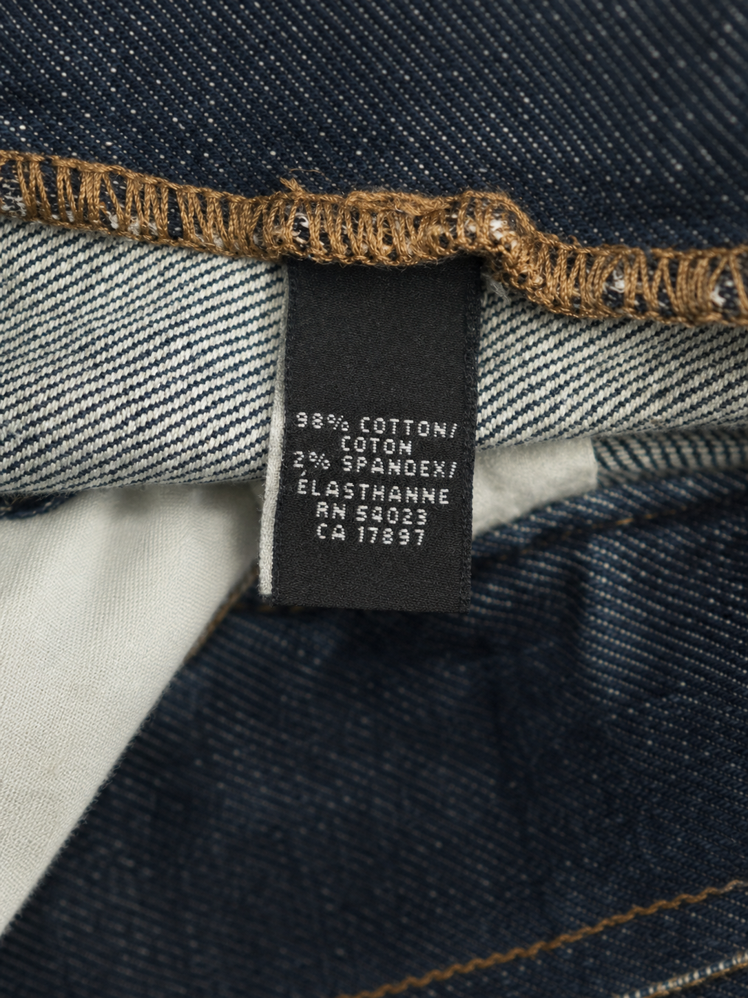 Close-up of a dark blue denim garment showing the inner label with fabric composition details, including '98% COTTON / COTON 2% SPANDEK / ÉLASTHANNE'.