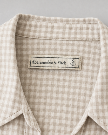 Close-up of a collared shirt with a beige and white gingham pattern, featuring an Abercrombie & Fitch brand label on the inner neck.